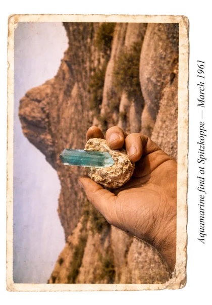 A large aquamarine being held aloft by a miner with Spitzkoppe in the background